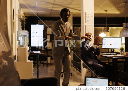 Cheerful happy worker having fun in startup office, listening music while showing funny dance moves. Executive manager working overtime at company investment plan. Business concept 107090126