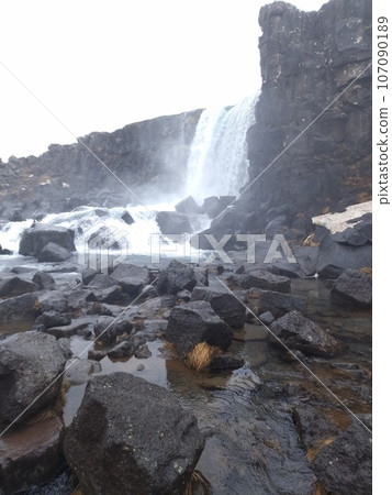 Gullfoss waterfall in nordic landscape, majestic icelandic scenery with snowy hills and icy water falling off cliff. River stream on top of frosty rock mountains, scandinavian cascade near valley. 107090189