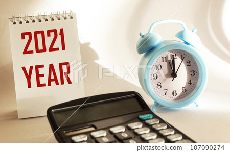 On a white background calendar with the text 2021 year, next to an alarm clock and a calculator 107090274