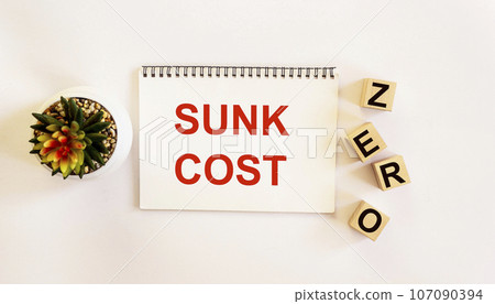 Notepad with the text SUNK COST on a white background. And the word ZERO on the cubes Notepad with the text SUNK COST on a white background. And the word ZERO on the cubes 107090394