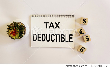 Tax deduction written on a notebook, next to cubes with dollar and euro symbols Tax deduction written on a notebook, next to cubes with dollar and euro symbols 107090397