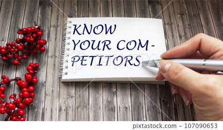 KNOW YOUR COMPETITOR. Wooden table with writing message by female hand KNOW YOUR COMPETITOR. Wooden table with writing message by female hand 107090653