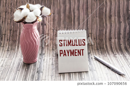 The Stimulus Payment incentive is written in a notepad on a wooden table next to a vase  107090656