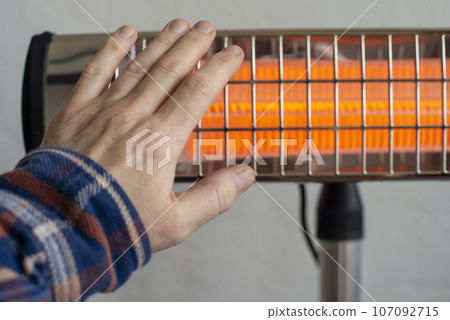 Caucasian male warming up hand near infrared heater. Space for text 107092715