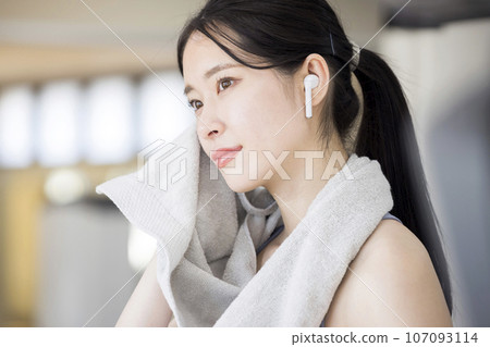 Young woman wearing wireless earphones wiping sweat at the gym 107093114