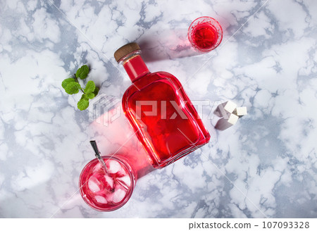 A bottle of red alcohol, a glass of liquor and an old-fashioned glass with an iced cocktail and a reusable straw. next to a sprig of mint and three pieces of sugar for absinthe. On a marble backgrou A bottle of red alcohol, a glass of liquor and an old-fashioned glass with an iced cocktail and a reusable straw. next to a sprig of mint and three pieces of sugar for absinthe. On a marble backgrou 107093328