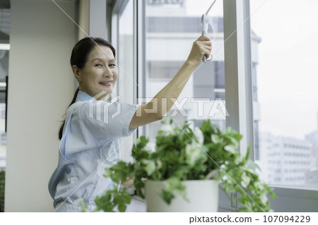 Senior female cleaner cleaning windows in the office 107094229
