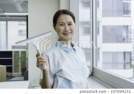 Portrait of a senior female cleaner cleaning windows in an office Portrait of a senior female cleaner cleaning windows in an office 107094231