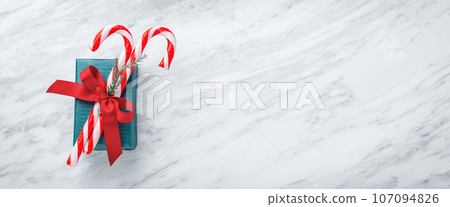 Green gift box with christmas candy cane and red bow on white marble background, top view, copy space 107094826