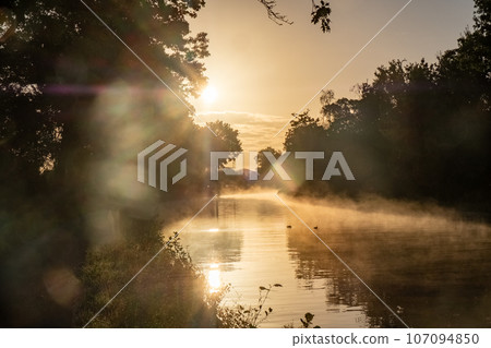 Mystical Sunset Mist Over Canal: Golden Rays Illuminating Tranquility 107094850