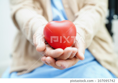 Asian elder senior woman patient holding red heart in hospital. 107095742