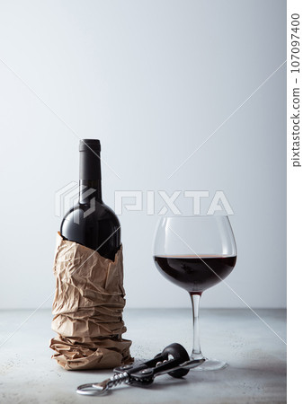 Bottle of wine in shopping paper bag with opener and glass of wine o light restaurant background. 107097400