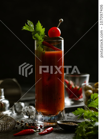 Bloody mary cocktail with red hot peppers and celery on wooden board with bar shaker 107097406