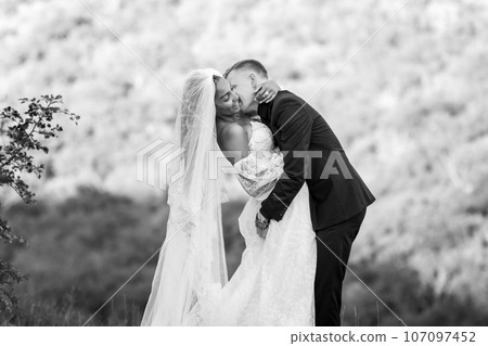 Happy newlyweds hugging against the backdrop of evening sunny foliage, black and white version 107097452