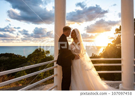 Portrait of newlyweds in a gazebo with columns in the rays of the setting sun Portrait of newlyweds in a gazebo with columns in the rays of the setting sun 107097458