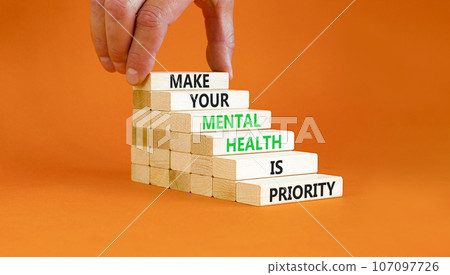 Mental health psychological symbol. Concept words Make your mental health a priority on wooden block. Beautiful orange table orange background. Businessman hand. Psychological mental health concept. 107097726