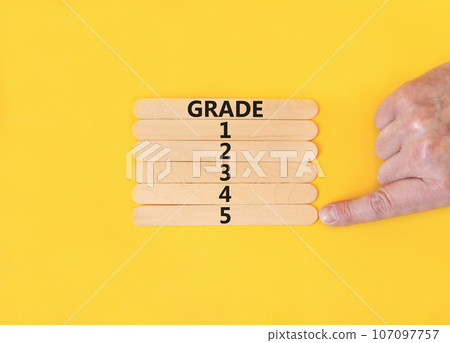Time to grade 5 symbol. Concept word Grade 1 2 3 4 5 on wooden sticks. Businessman hand. Beautiful yellow table yellow background. Business planning and time to grade 5 concept. Copy space. Time to grade 5 symbol. Concept word Grade 1 2 3 4 5 on wooden sticks. Businessman hand. Beautiful yellow table yellow background. Business planning and time to grade 5 concept. Copy space. 107097757