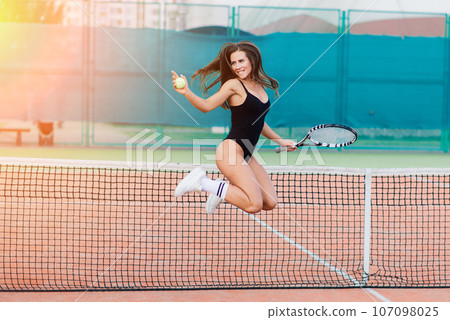 Beautiful young sport female dressed in bodysuit on tennis court 107098025