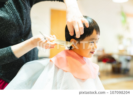 A 3-year-old boy getting a haircut at a beauty salon A 3-year-old boy getting a haircut at a beauty salon 107098204