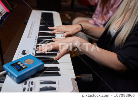 Closeup of female hands on an electronic piano. A laptop on a keyboard instrument. 107098966