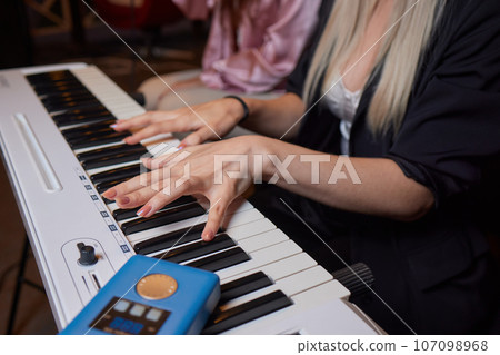 Closeup of female hands on an electronic piano. A laptop on a keyboard instrument. 107098968
