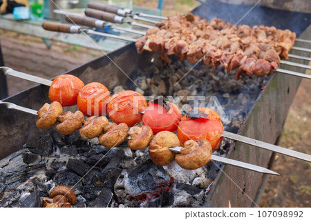 Closeup of marinated big turkey or chicken meat steak shashlik or shish kebab preparing cooking on barbecue brazier grill over charcoal on burning coal. Skewered roasted kebabs on BBQ grill 107098992