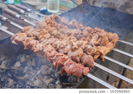 Closeup of marinated big turkey or chicken meat steak shashlik or shish kebab preparing cooking on barbecue brazier grill over charcoal on burning coal. Skewered roasted kebabs on BBQ grill 107098993