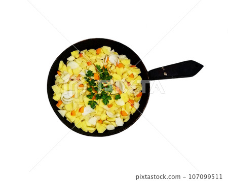 Raw chopped potatoes with onions, carrots and parsley for brewing in an old iron frying pan 107099511