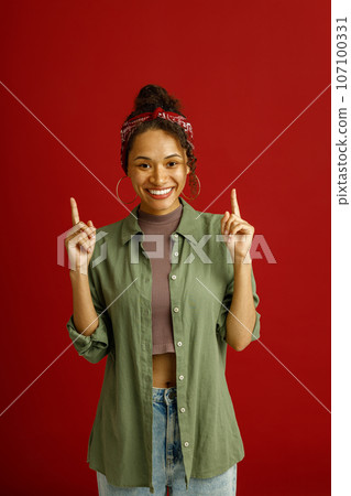Smiling young woman holding index fingers up with great new idea on red studio background 107100331