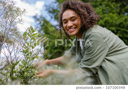 Positive female gardener takes care of plants while working in garden center Positive female gardener takes care of plants while working in garden center 107100349