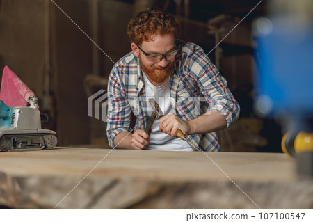 Close up of craftsman working with chisel while cutting wooden plank in carpentry workshop 107100547