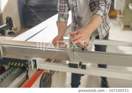 Close up of carpenter cutting wooden board at sawmill carpentry manufacturing . Sawing machine Close up of carpenter cutting wooden board at sawmill carpentry manufacturing . Sawing machine 107100551