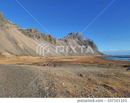 Famous vestrahorn mountains on beach with huge rocky hills in amazing nordic landscape and fields in Iceland. Stokksnes beach creating wintry natural setting, arctic ocean shoreline. 107101103
