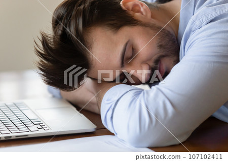Close up tired exhausted man sleeping at work desk Close up tired exhausted man sleeping at work desk 107102411