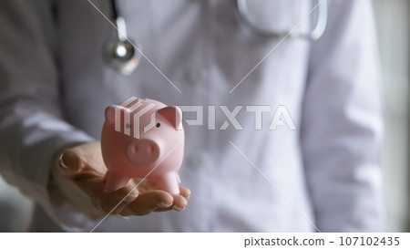 Close up of female doctor hold piggy bank Close up of female doctor hold piggy bank 107102435