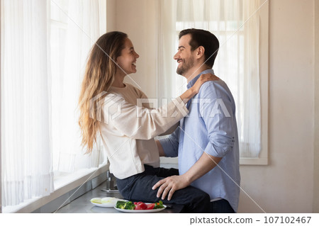 Beautiful woman sitting on countertop, having fun with husband Beautiful woman sitting on countertop, having fun with husband 107102467