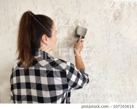 Woman with putty knife doing renovations in the apartment. 107103618