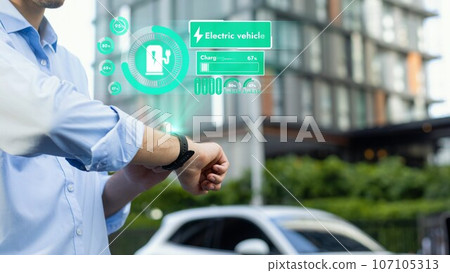 Businessman checking EV car battery status in hologram from smartwactch. Peruse 107105313