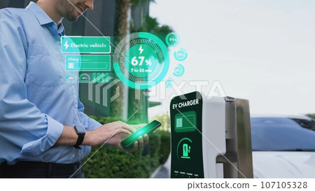 Businessman checking battery status hologram from EV smartphone. Peruse Businessman checking battery status hologram from EV smartphone. Peruse 107105328