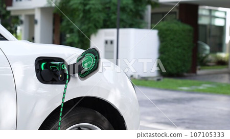 Electric car plugged in with home charging station. Peruse Electric car plugged in with home charging station. Peruse 107105333