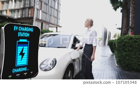 Businesswoman recharge her electric car from charging station. Peruse Businesswoman recharge her electric car from charging station. Peruse 107105348