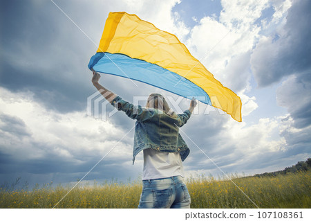 woman with Ukrainian flag in rapeseed field. waving national flag praying for peace. Happy girl celebrating Independence Day. 107108361
