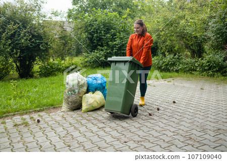 Adult woman household taking out bin to the street on rubbish day. 107109040
