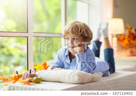 Child at window in autumn. Kids at home in fall. Child at window in autumn. Kids at home in fall. 107110402