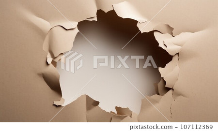 Hole in cardboard paper with torn edges 107112369