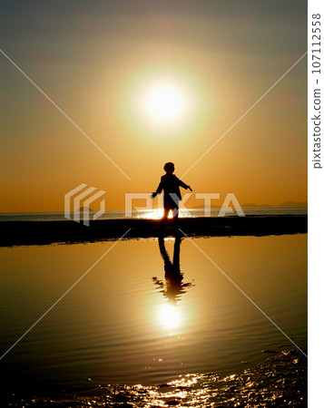 夕陽西下，一個人站著伸出雙手的剪影，影子倒映在水面上 107112558