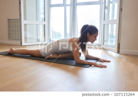 Young athletic attractive woman practicing yoga doing exercises. Works out at home or in a yoga studio, sportswear, blue pants and a full-length top indoors. Healthy lifestyle concept. 107115264