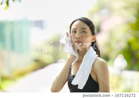 穿著運動服的年輕女子在綠色植物中用毛巾擦汗 穿著運動服的年輕女子在綠色植物中用毛巾擦汗 107116272