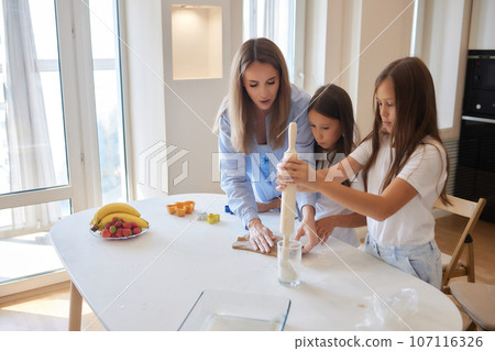 Close up image woman and little daughter knead dough with hands wooden table powdered with flour. 107116326