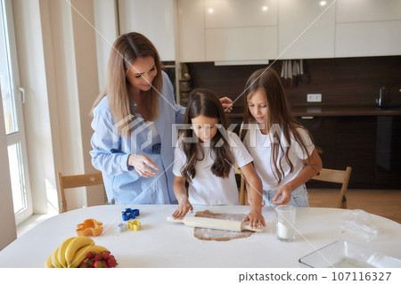 Close up image woman and little daughter knead dough with hands wooden table powdered with flour. 107116327